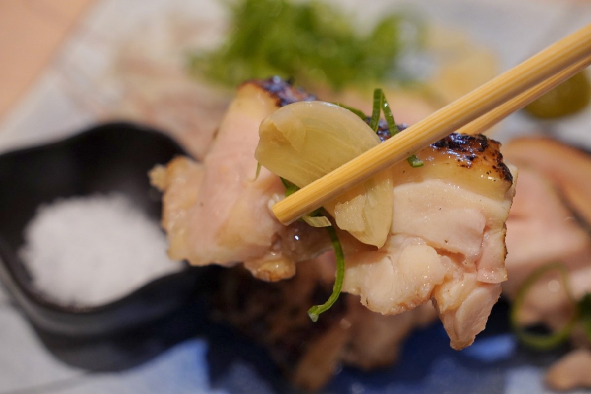 薬味を添えた大山どり麹漬け藁焼きを箸で持ち上げた様子